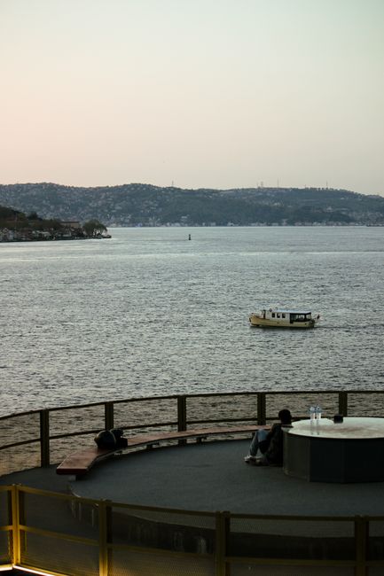 Couple enjoys serene sunset view over Istanbul's Bosphorus with distant hills and boat.