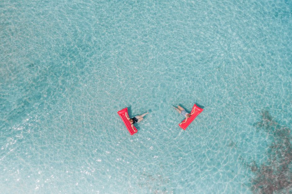 Two adults on red inflatables relax in clear turquoise waters of Hawaii. Aerial capture.